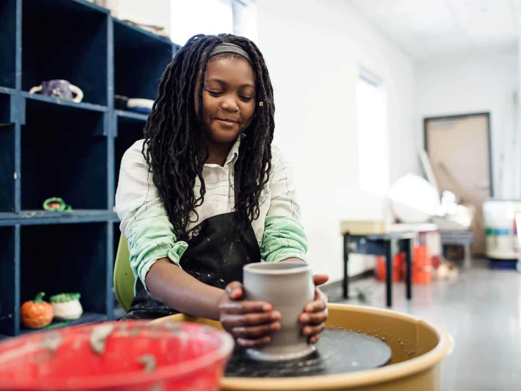 girl shaping pottery on spinning wheel