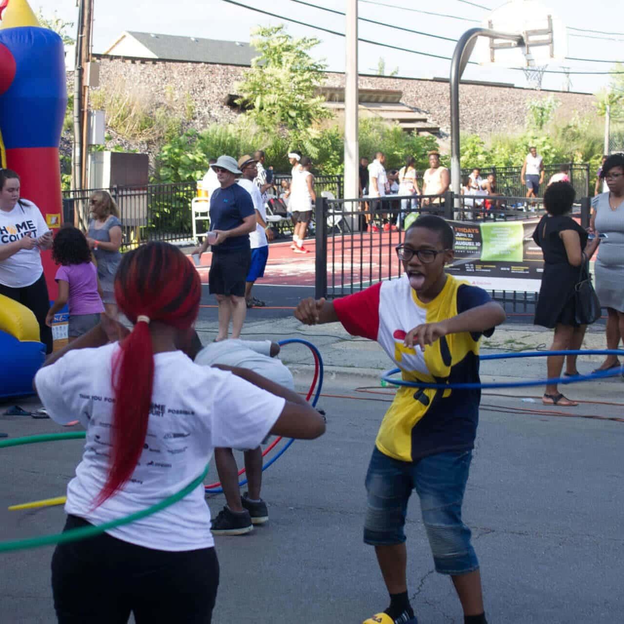 kids hula-hooping at Breakthrough Homecourt event in front of bounce house and basketball court