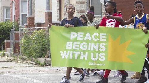 youth marching down East Garfield Park street holding Peace Begins With Us banner