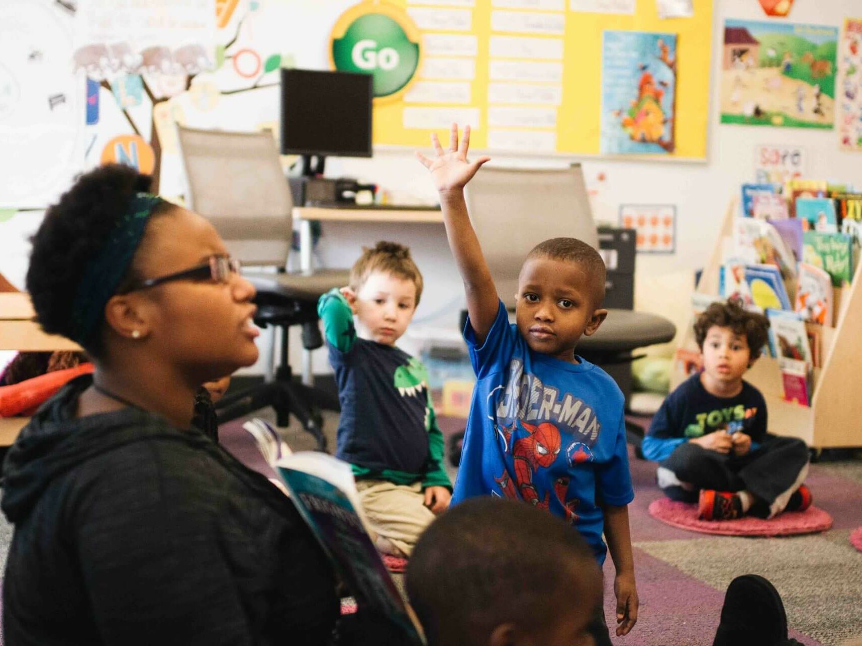 boy raising his hand to answer a question in preschool class